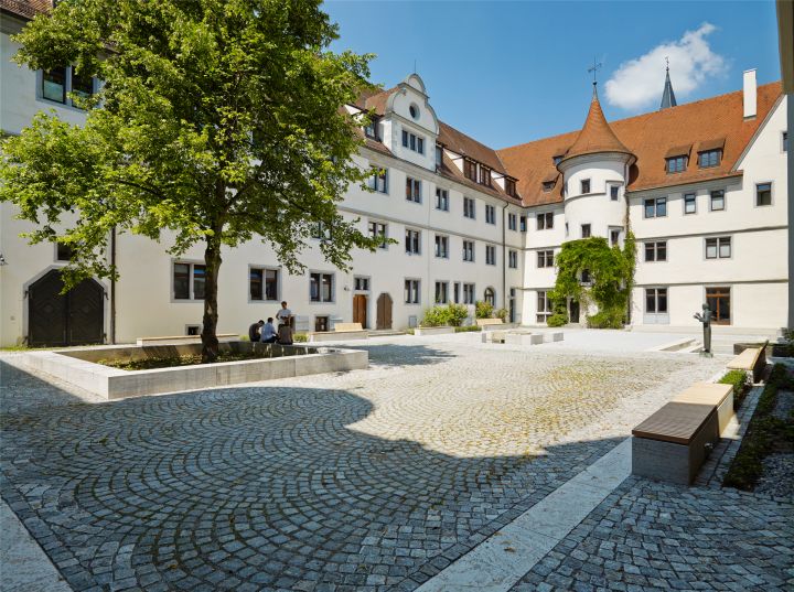 Das Wilhelmsstift in Tübingen im sanierten Zustand im hinteren Bildbereich, mit Freiflächen und Sitzgelegenheiten im vorderen Bildbereich.