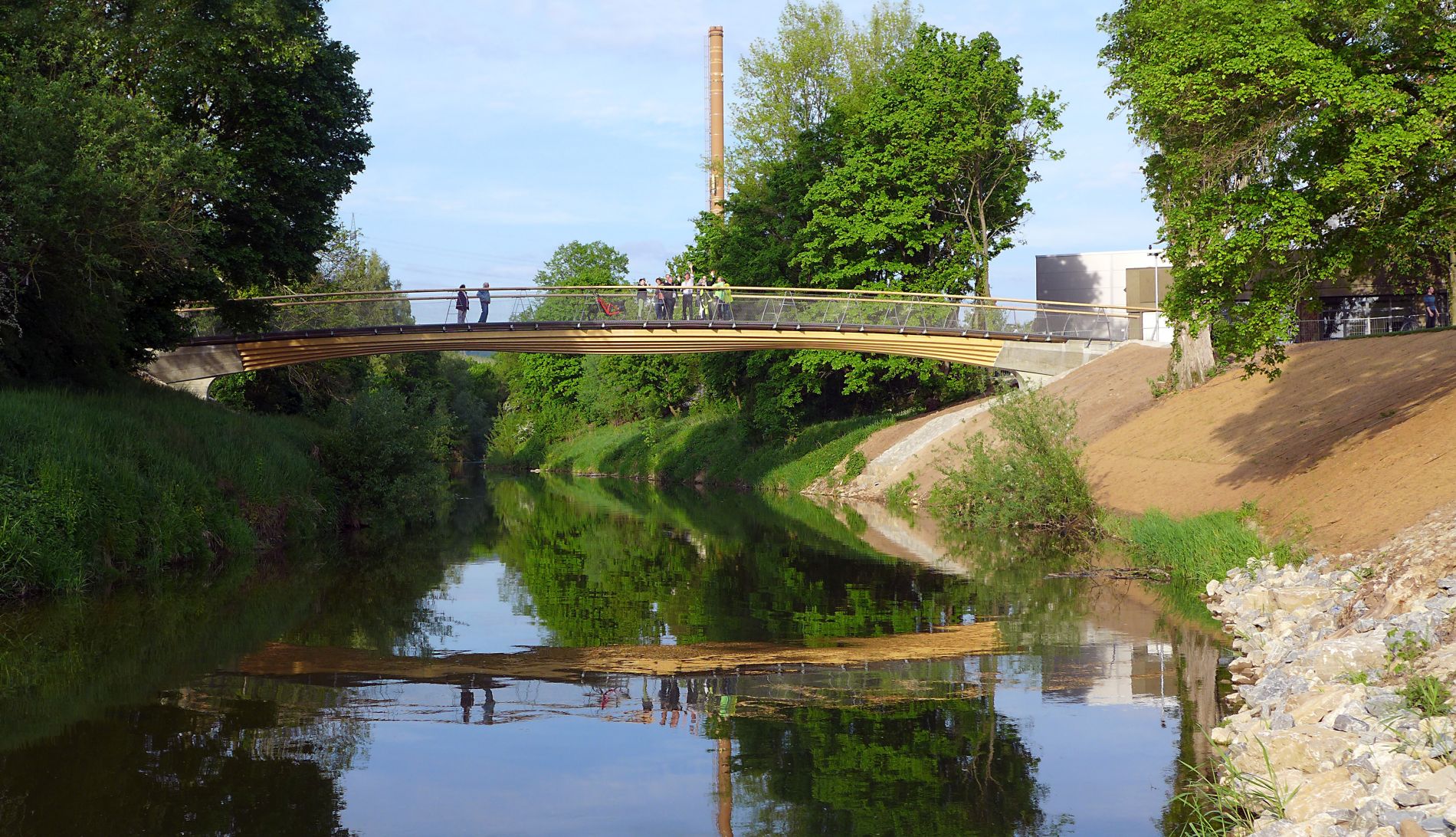 Eine filigrane elegante Brücke aus schichtweise und abgetreppt angeordneten Holzbrettern als tragender Konstruktion spannt sich von Ufer zu Ufer über den Fluss Rems.