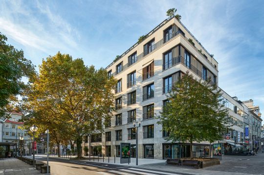 Die steinerne Lochfassade mit bodentiefen Fenstern und die zweigeschossige Aufstockung in leichter Holzbauweise mit Rooftop-Bar lassen die Fassade des ehemals konventionellen Bürogebäudes aus den 1960er Jahren in neuem Glanz erstrahlen. 