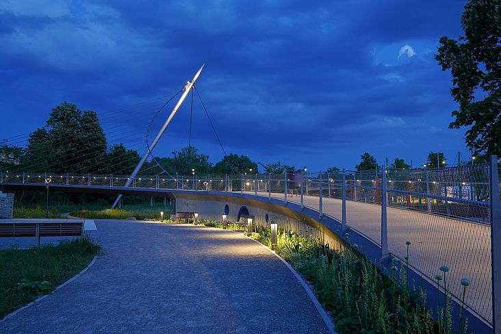 Die mit seilgespannte Fußgängerbrücke und Stahlbetonrampen verbindet die beiden Stadtteile und gibt gleichzeitig den Blick frei auf die Enzaue. 