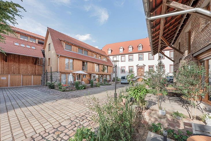 Sanierung der historischen Hofanlage unter Verwendung historischer Materialien wie alte Mauer- und Pflastersteine zum  Erhalt des Erscheinungsbildes der Gebäude im mittleren Teil des Bildes erkennbar.
