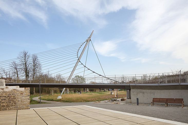 Die mit seilgespannte Fußgängerbrücke und Stahlbetonrampen verbindet die beiden Stadtteile und gibt gleichzeitig den Blick frei auf die Enzaue. 